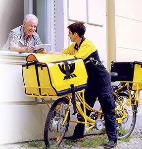 Ein Mann überreicht durchs Fenster einer Postbotin mit Fahrrad einen Brief